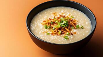 Warm autumn Asian dish featuring a bowl of savory pumpkin congee, topped with crispy shallots and fresh green onions, set against a gradient background shifting from burnt orange to deep brown photo