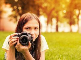 joven mujer fotógrafo con cámara mentira abajo en césped. imagen con copyspace y besado por el Sol efecto. atención a cámara. superficial dof foto