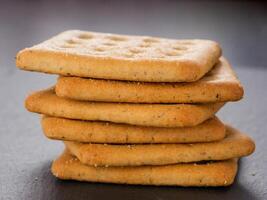 stack of square crackers on slate gray background. Dry salt cracker cookies with fiber and dry spices photo