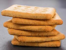 stack of square crackers on slate gray background. Dry salt cracker cookies with fiber and dry spices photo