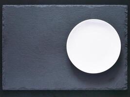 Empty white plate on black slate board on dark background. Flat lay or top view. Can use fo design menu photo