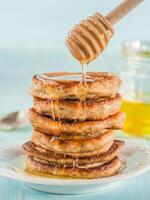 Stack of small pancakes with banana and chia seeds in honey on light blue background. Honey pouring over stack of mini pancakes with chia or poppy seeds. photo
