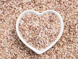 Red rice in heart-shaped bowl on rice background photo