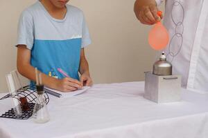 Student study to do science experiment about reaction of air in balloon with water filled is burned on fire flame of metal lantern. Concept, science lesson, activity at school. photo