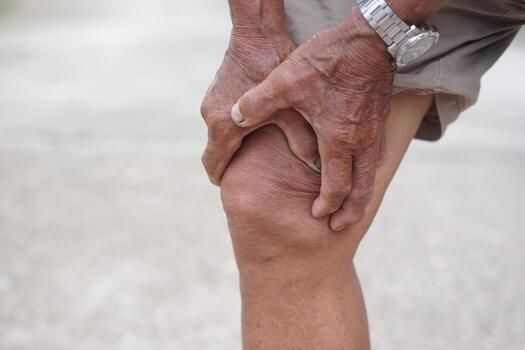 Close up elderly man hurt his knee, use hands to massage knee. Concept, health care and health problems. Artritis symptom. Suffering from knee pain. Tendon problems and Joint inflammation photo