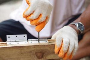 Close up carpenter hands are installing hinge on wooden window. Concept, Craft, diy, fix or repair furniture. Building materials. Construction equipment. Install in door or window, cabinet or others. photo