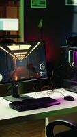 Vertical Computer screen showing FPS videogame left open at night in empty apartment with RGB lights. Close up shot of PC, keyboard and mouse on desk in living room with no people in video