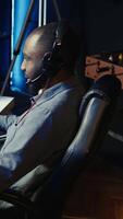 Vertical Man using headset to play SF FPS videogame, having fun in dark apartment room. Gamer competing in PvP online multiplayer game, shooting other players with futuristic gun, camera B close up video