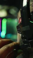 Vertical Man playing SF videogame on computer, having fun in neon lit apartment, close up. Gamer competing in online multiplayer game, using headphones to talk with teammates, camera B video