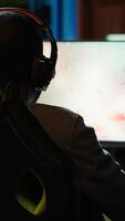 Vertical Pro gamer wearing headphones playing science fiction game. Content creator in gaming chair talking with audience on headset mic, filming tutorial on how to defeat enemies, camera A video