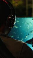 Vertical Gamer using headphones to discuss with mates while playing online SF videogame, close up. Close up enjoying futuristic coop spaceship flying arcade game with friends, chatting on internet, camera A video