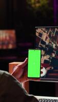 Vertical Isolated screen smartphone held by player competing in online multiplayer videogame at home. Mockup mobile phone utilized by person playing on gaming PC in neon illuminated apartment video