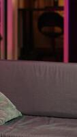 Vertical Man arriving home, gaming and enjoying leisure time. Man sitting on couch in neon illuminated living room, playing videogame on console, relaxing after hard day at work, camera A video