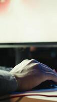 Vertical Gamer using keyboard and wired mouse to play videogames on desktop PC, close up shot. Man playing online game in front of monitor with computer peripherals at desk in apartment, camera B video