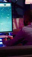 Vertical Gamer using controller and headphones to play first person shooter videogame on large smart TV. Man in home theatre using high tech gaming console gamepad to defeat foes, camera A video