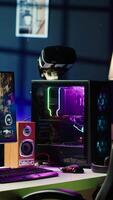 Vertical RGB lights illuminated components on open gaming PC tower next to computer peripherals, display and VR headset in empty apartment. Desktop PC in home living room, monitor and virtual reality glasses video
