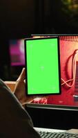Vertical Man watching videos on green screen tablet while playing first person shooter videogame at home. Gamer looking at chroma key device display while enjoying online game on PC