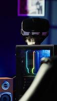 Vertical RGB lit parts on opened gaming PC tower next to keyboard, stereo speakers, display and high tech VR headset in empty apartment. Computer with modern hardware, monitor and virtual reality glasses video