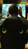 Vertical African american player in neon illuminated apartment paying close attention to computer screen during videogame competitive match. Person competing in internet esports tournament, camera B video