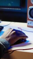 Vertical Keyboard and mouse used by gamer competing in online multiplayer videogame at home, close up. Focus on computer peripheral utilized by man playing on gaming PC in neon illuminated apartment, camera A video