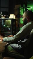 Vertical Man in neon lit apartment playing immersive games on gaming PC at computer desk, handheld camera shot. Gamer competing against enemies in internet multiplayer shooter, camera B video