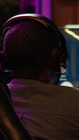 Vertical Pro gamer wearing headphones playing game, teaching audience esports needed skills. Content creator in gaming chair talking with audience, filming tutorial on how to defeat enemies, camera A video