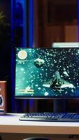 Vertical Man playing SF space videogame on PC screen in neon illuminated apartment living room. Gamer enjoying spaceship flying game on computer desktop display in RGB lit home late at night, camera A video