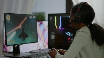 Pro african gamer playing online space shooter game on powerful computer using wireless controller and headset. Competitive cyber player woman performing videogame tournament use professional joystick video