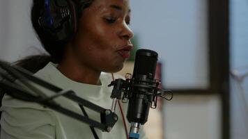 Close up of afro woman vlogger making new blog in home studio talking in professional microphone with audience. Speaking during livestreaming, blogger discussing in podcast wearing headphones. video
