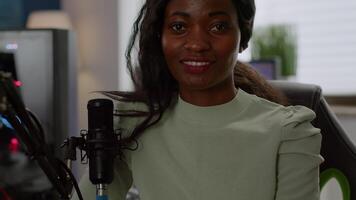 Black woman gamer looking at camera smiling and playing virtual shooter game championship in cyberspace, esports player performing on powerful computer in stylish room during gaming tournament video