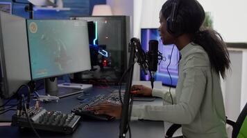 Competitive black gamer with headphones using stream chat on RGB powerful computer playing online shooter game late at night. Virtual online streaming cyber performing in gaming tournament video