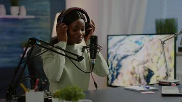 African blogger smiling at audience while filming podcast, looking at camera putting on headset. On-air production internet broadcast host streaming live content, recording digital social media video