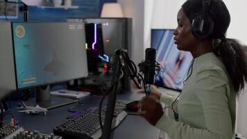 African woman streamer cyber putting on headphones performing space shooter game on RGB powerful computer talking with players on stream chat, with microphone in gaming competition. video