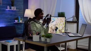 African blogger influencer putting on headset and smiling before recording blog, looking at camera. Social media content creator speaking during livestreaming, blogger discussing in podcast video