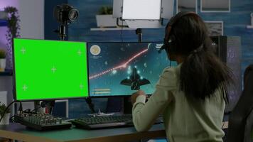 African gamer playing virtual videogame on powerful computer, chatting on green screen mock up, chroma key display. Cyber player using pc with isolated desktop streaming shooter games wearing headset video