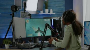Black woman streamer playing space shooter videogames with joystick talking with teammates on streaming open chat. Cyber performing on RGB powerful computer in gaming room using professional equipment video