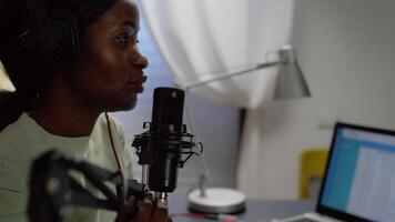 Close up of african blogger woman speaking at microphone during podcast using professional recording technology in home studio. Content creator making serires for channel, streaming online broadcast video