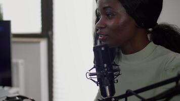 Portrait of african cyber talking on stream chat with players using micorphone and powerful computer. Streamer woman sitting on chair playing space shooter game during online esports tournament. video
