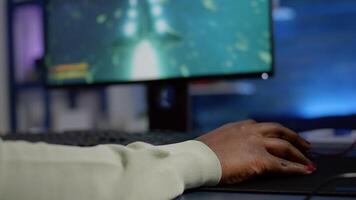 Close up of african woman cyber moving professional mouse with RGB playing space shooter game. Player using powerful gaming computer in home studio of esport videogame typing at keypad video