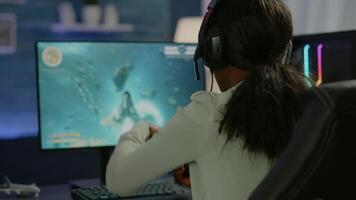 Closeup of competitive black woman player holding joystick playing space shooter game at powerful computer late night. Professional gamer using wireless controller for online gaming championship video