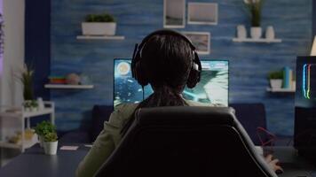 Back shot of streamer woman playing on RGB powerful computer shooter game for tournament, talking with multiple players into headphones. Pro gamer using professional streaming equipment video