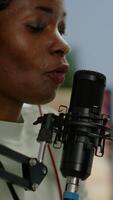Vertical . Close up of afro woman vlogger making new blog in home studio talking in professional microphone with audience. Speaking during livestreaming, blogger discussing in podcast wearing headphones. video