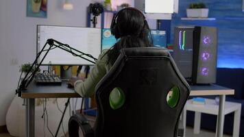 Back shot of streamer woman playing on powerful computer shooter game for tournament, talking with multiple players into headphones. Pro gamer using professional streaming equipment video