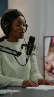Vertical . Smiling social media star sitting in front of camera waving and filming for youtube channel using smartphone. Vlogger speaking and recording online talk show at home studio for digital podcast video
