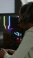 Vertical . Pro african gamer playing online game on powerful computer using wireless controller and headset. Competitive cyber player woman performing videogame tournament use professional joystick video