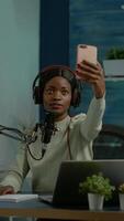 Vertical . African content creator taking photo with smartphone for fans and recording broadcast. On-air online production internet podcast show host streaming live content, recording digital social media. video