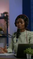 Vertical . African social media woman looking in laptop talking at microphone recording podcast for youtube channel using camera. Online show On-air production internet broadcast host streaming live video
