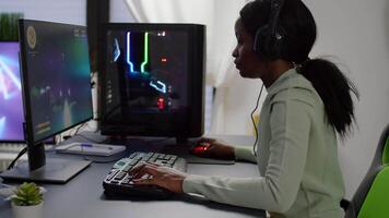 Happy black gamer raising hands winning space shooter online competition talking at professional microphone in gaming studio. Gamer playing online game with streaming chat open during tournament video