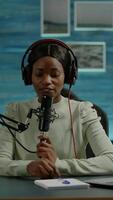 Vertical . Famous young african woman recording a vlog for subscribers using podcast microphone for vlogging. On-air online production internet broadcast show host streaming live content for social media video