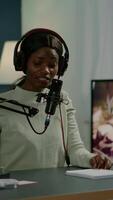 Vertical . Famous vlogger making online podcast recording for virtual show in front of camera. Influencer using headphones speaking at microphone. On-air production internet broadcast show host streaming video